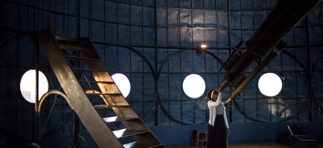 Fatoumata Kebe looks into a telescope in a dark observatory