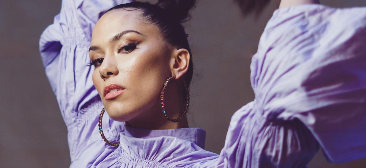 Thais Lona holding her braid in a purple dress looking at the camera