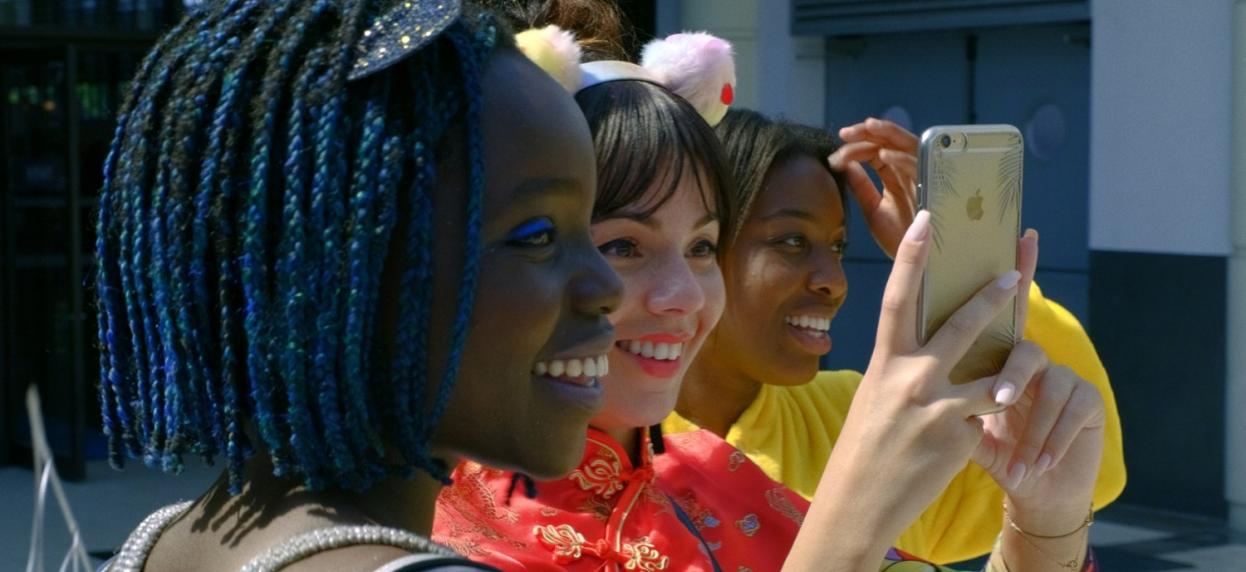 Three young women smile and take a picture of something in the distance
