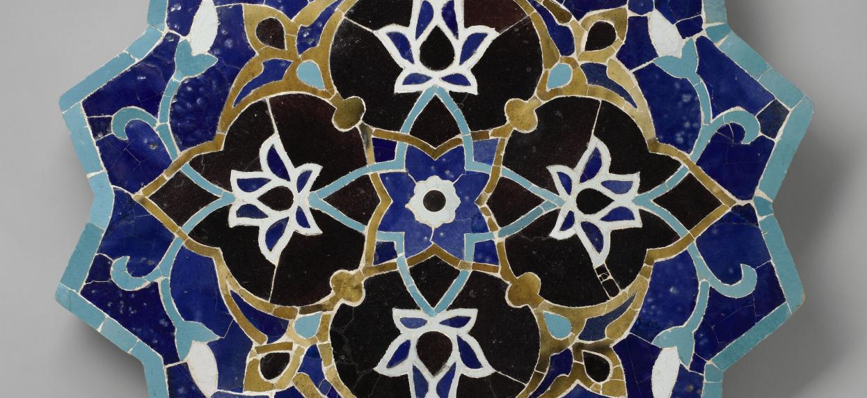 Fragment d'une décoration architecturale en forme étoilée avec des arabesques dorées et des nuances de bleu et de noir.