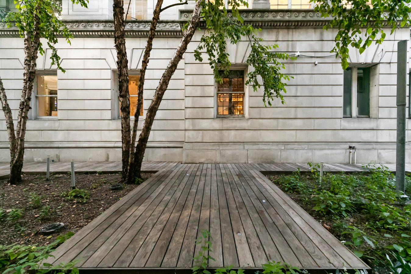 The Florence Gould Garden outside the Payne Whitney Mansion, featuring wooden walkways and several large trees facing the south side of the building.