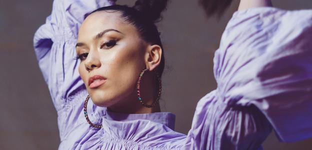 Thais Lona holding her braid in a purple dress looking at the camera