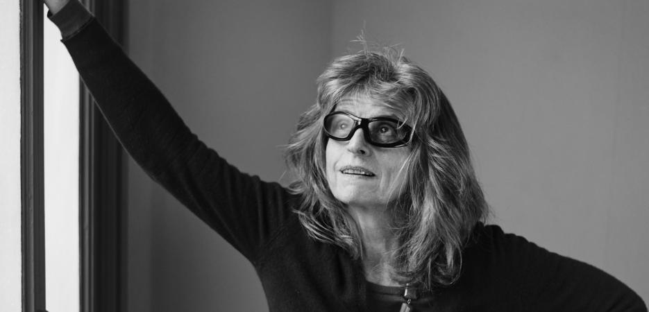 Black and white image of Claire Simon standing up leaning against a door